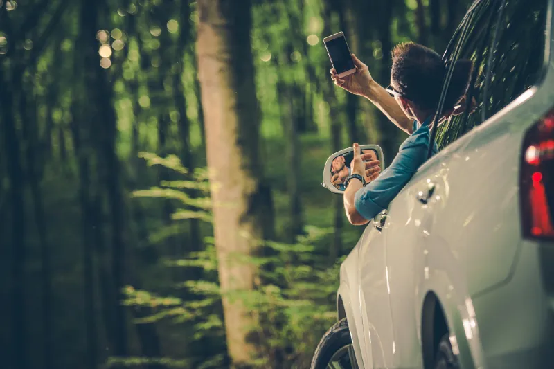 Uomo controlla il segnale cellulare accanto a un’auto in una zona boschiva